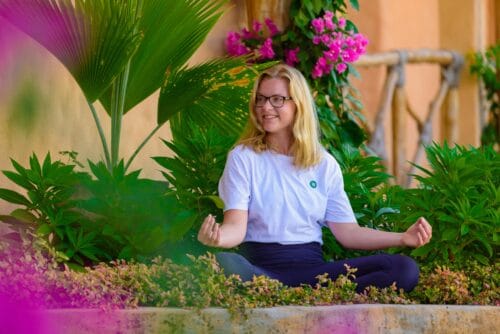 Cathrine sidder klar til at mediterer omringet af smukke blomster i haven på yogarejse til Zanzibar