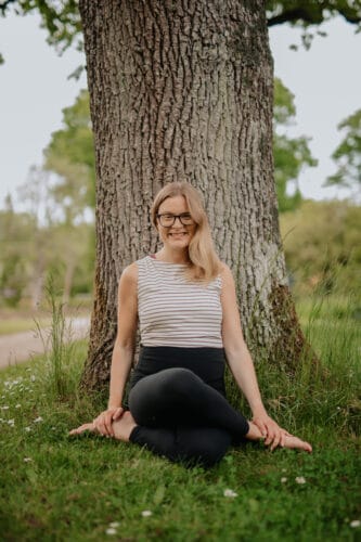 Cathrine laver yin yoga øvelsen knudeben foran et stort træ