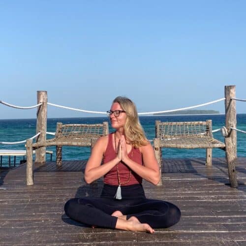 Cathrine sidder på en bro ved havet og mediterer på yogarejse til Zanzibar
