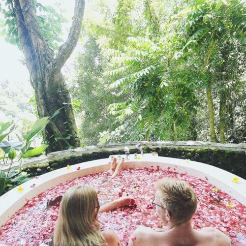 Tommy og Cathrine i udendørs badekar fyldt med blomsterblade og udsigt til junglen på Yogarejse til Bali