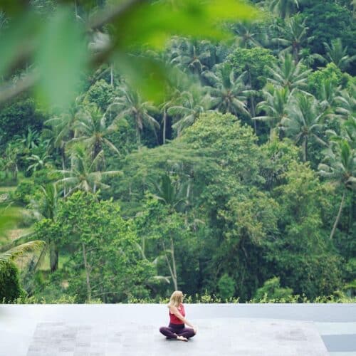Cathrine laver et siddende yogatwist udenfor med udsigt til junglen på Bali
