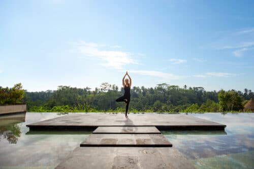 Yogaelev i træet stilling med pool og jungle som baggrund på Yang yogauddannelse på Bali