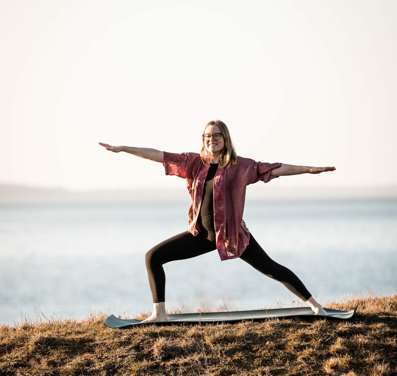 Cathrine står ved havet og laver yoga solhilsner der giver energi